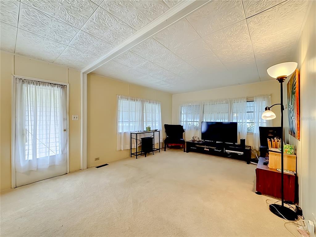 A living room features beige carpeting, a textured white ceiling, and a television on a stand — 4676 66TH LANE N UNIT 20, ST PETERSBURG, FL