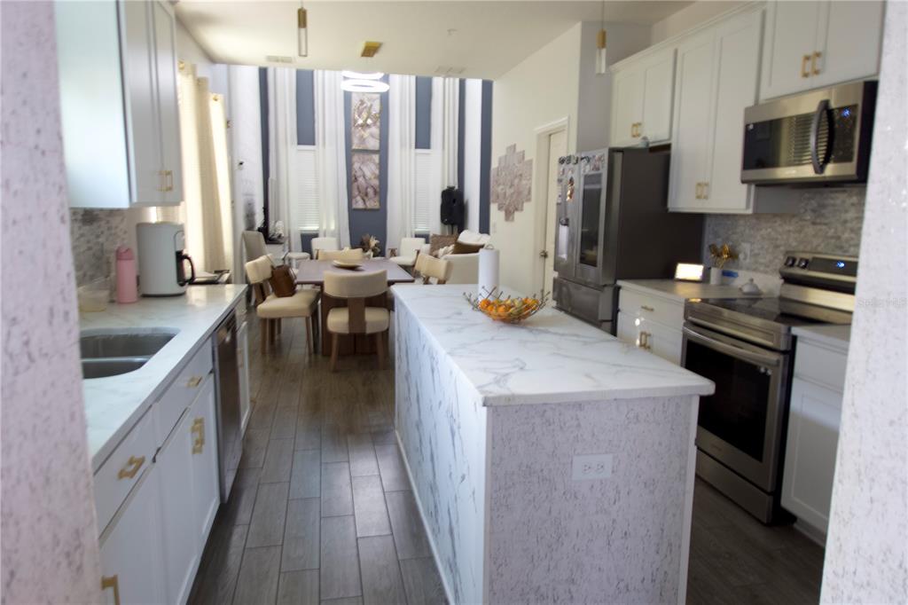 A kitchen with white cabinets, marble-look countertops, and an island opens to a dining area — 9803 AMBER CHESTNUT WAY, WINTER GARDEN, FL