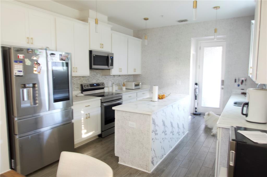 A kitchen features white cabinetry, stainless steel appliances, a marble-topped island, and wood-look tile flooring — 9803 AMBER CHESTNUT WAY, WINTER GARDEN, FL