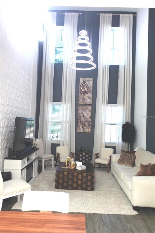 A living room features high ceilings, a modern ring chandelier, and a textured accent wall — 9803 AMBER CHESTNUT WAY, WINTER GARDEN, FL