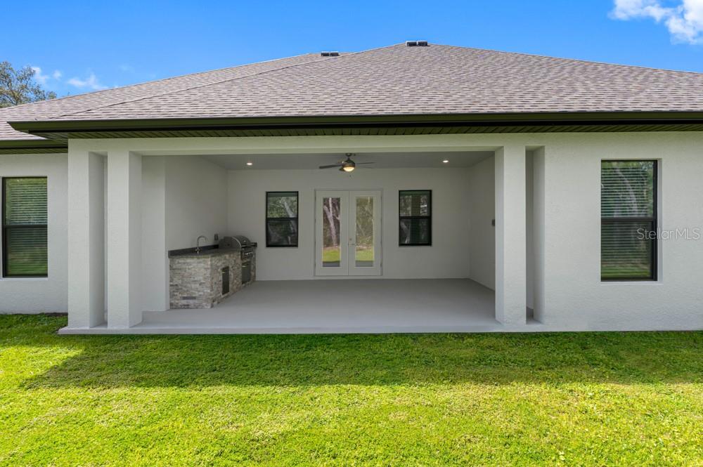 A covered patio features a stone-faced outdoor kitchen, double glass doors, and a ceiling fan — 17444 NOKOTA AVENUE, HUDSON, FL