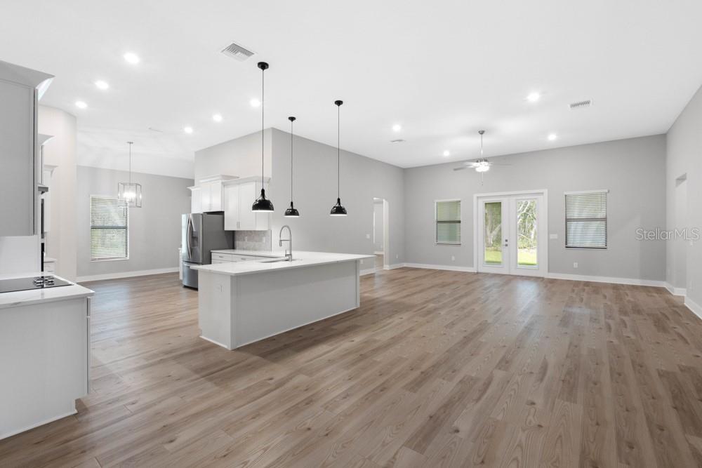 A bright, open-concept kitchen and living area featuring white cabinetry, a large island, and flooring — 17444 NOKOTA AVENUE, HUDSON, FL