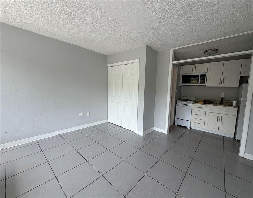 A room with gray tile flooring, a white closet, and an adjacent small kitchen area — 515 BON AIR STREET UNIT 160, LAKELAND, FL
