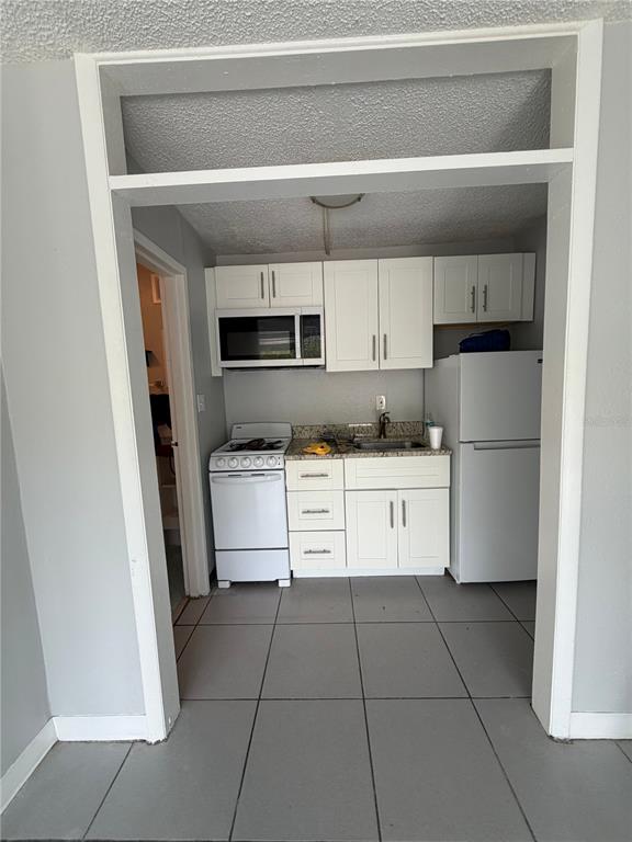 A small kitchen features white cabinets, a white stove, a refrigerator, and gray tile flooring — 515 BON AIR STREET UNIT 160, LAKELAND, FL