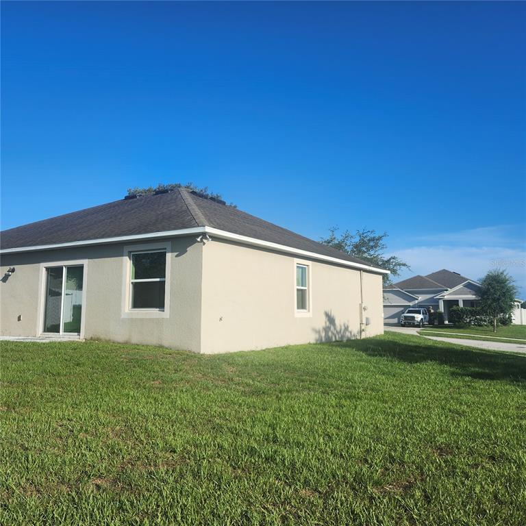 The exterior of a tan stucco house with a dark shingled roof and grass yard — 15548 GEMINI DRIVE, MASCOTTE, FL