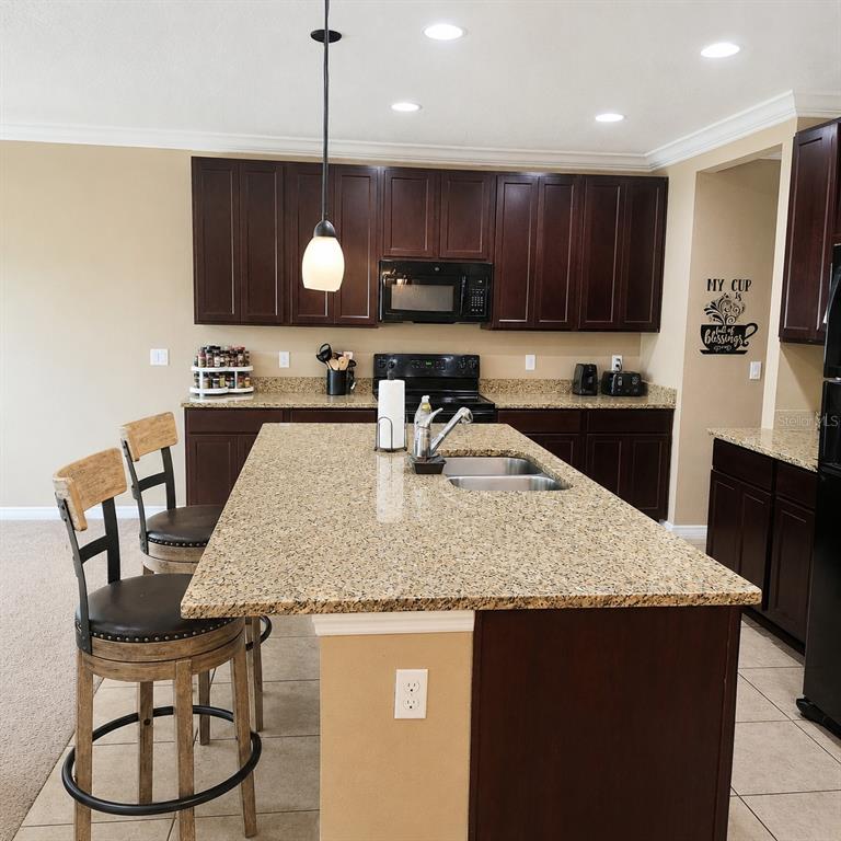 A kitchen features dark wood cabinets, granite countertops, a central island with a sink, and barstools — 15548 GEMINI DRIVE, MASCOTTE, FL