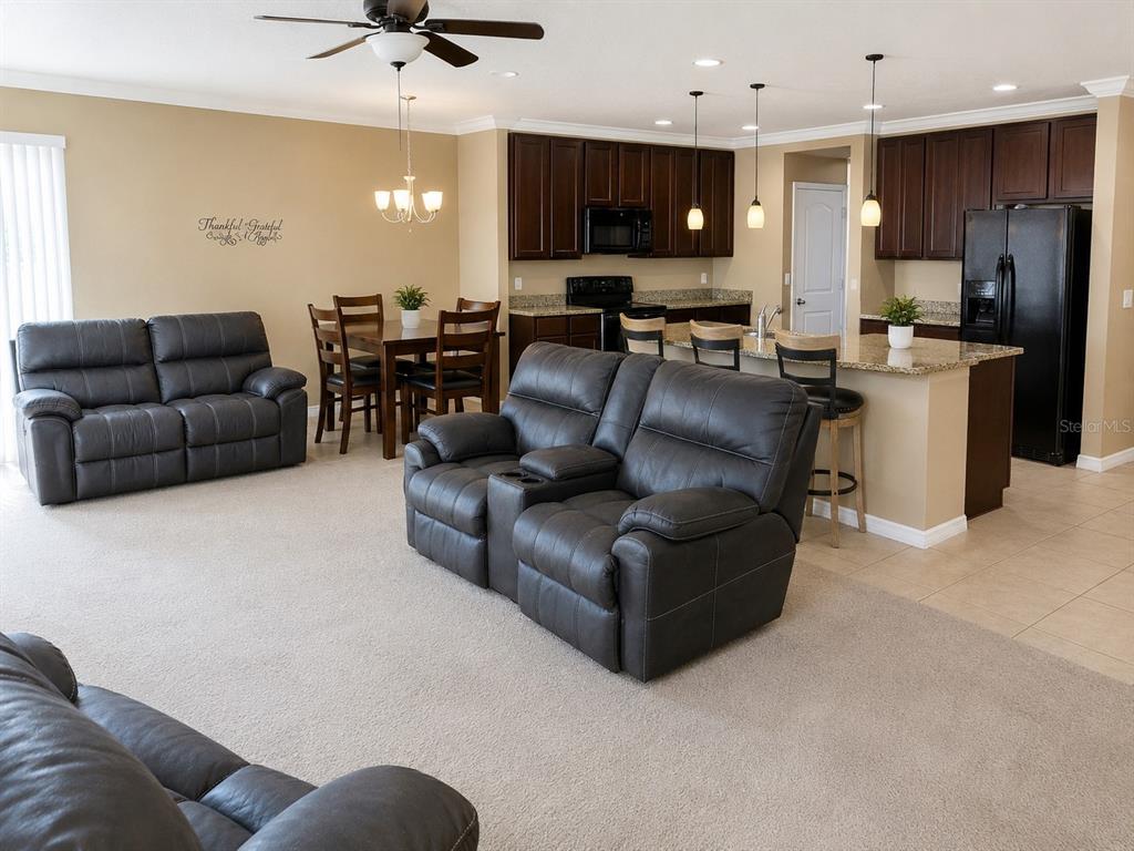 An open-concept living room, dining area, and kitchen with dark cabinetry and leather furniture — 15548 GEMINI DRIVE, MASCOTTE, FL