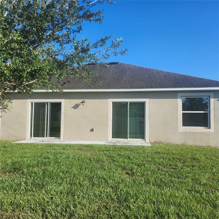The back exterior of a house features two sliding glass doors and one window — 15548 GEMINI DRIVE, MASCOTTE, FL