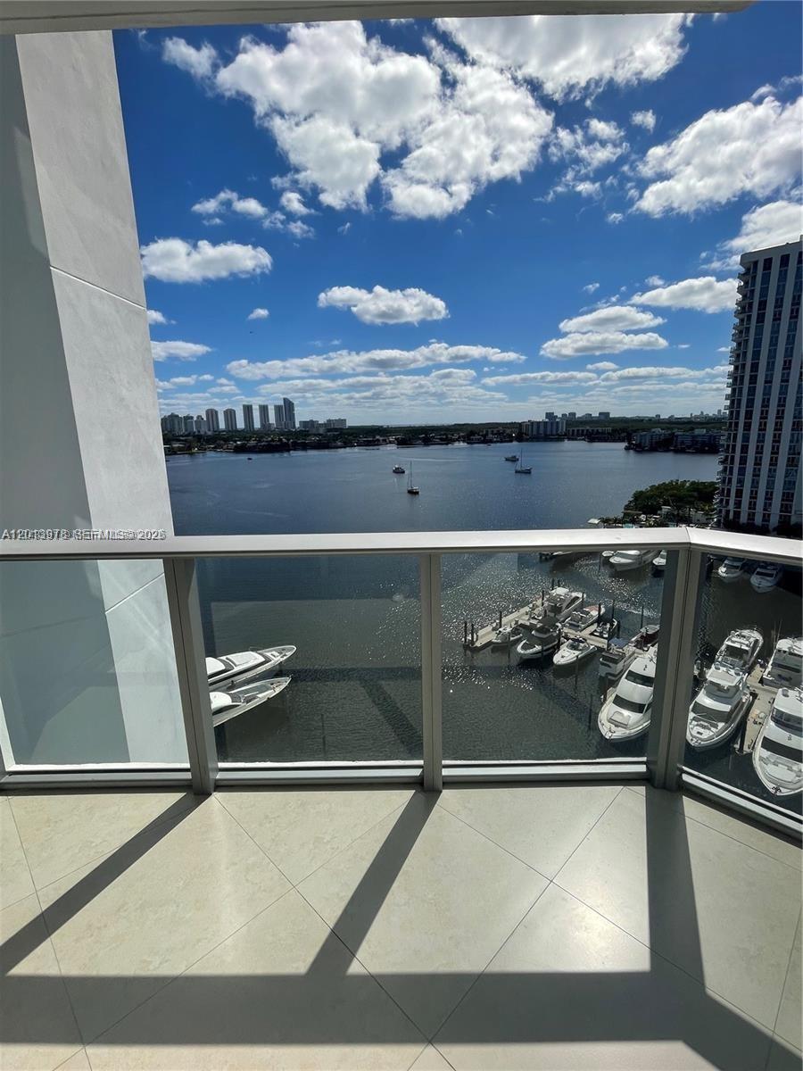 A balcony with a glass railing overlooks a marina and a bay under a cloudy sky — NORTH MIAMI BEACH, FL