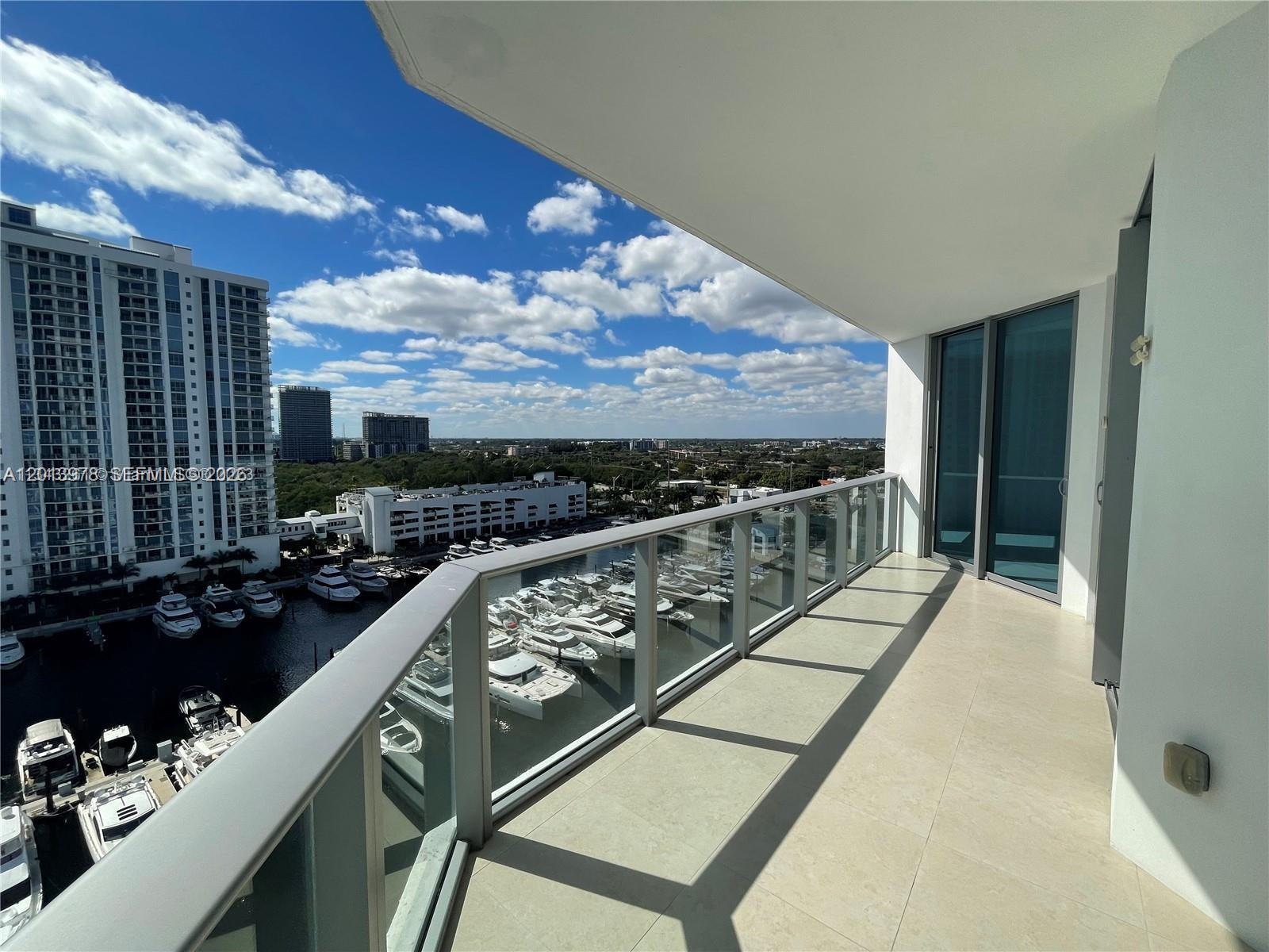 A balcony with a glass railing overlooks a marina and city skyline under a blue sky — NORTH MIAMI BEACH, FL