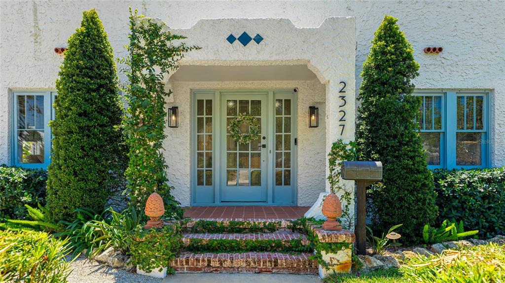 The front entrance of a stucco house features a glass-paned door, brick steps, and topiaries — 2327 7TH AVENUE W, BRADENTON, FL