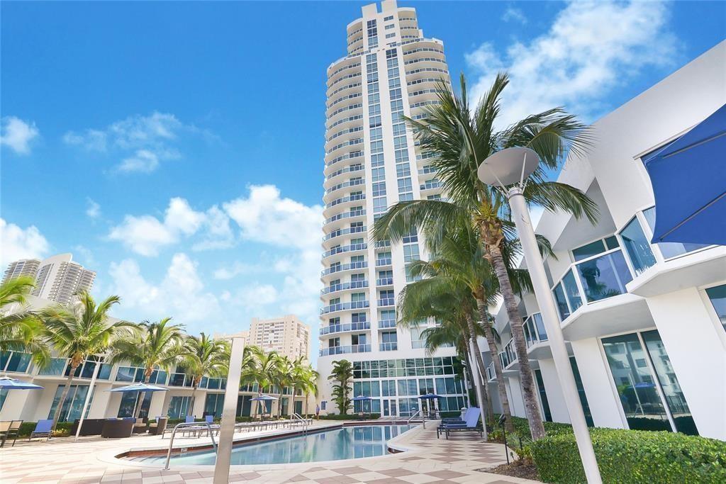 A tall white residential tower overlooks a swimming pool surrounded by palm trees and patio — 1945 S Ocean Drive # 910, Hallandale Beach FL 33009, HALLANDALE BEACH, FL