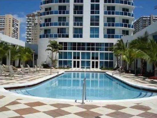 A swimming pool sits in front of a tall, white multi-story building with balconies — 1945 S Ocean Drive # 910, Hallandale Beach FL 33009, HALLANDALE BEACH, FL