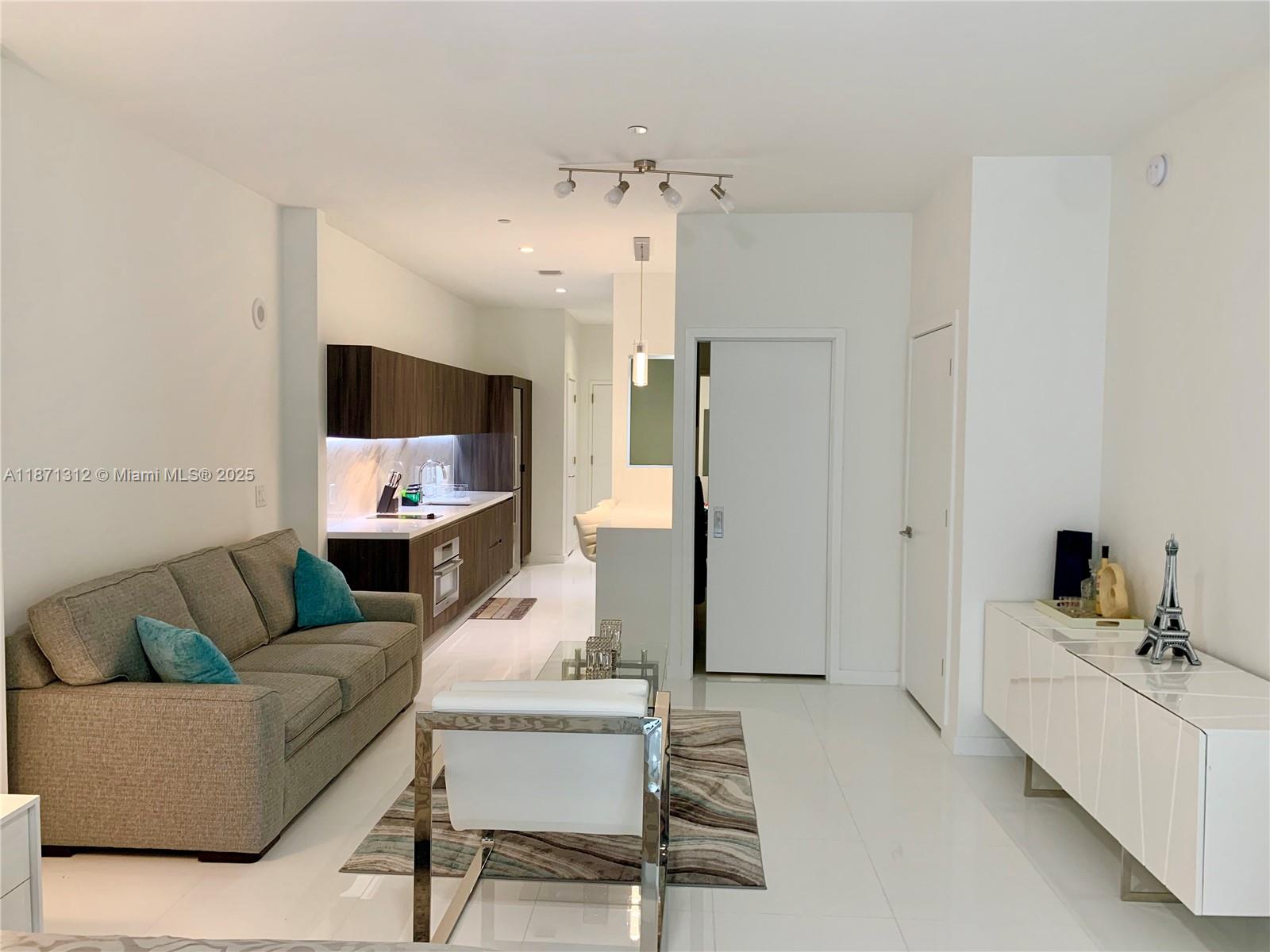 A modern living room features a grey sofa, white tile floors, and an adjacent kitchen — 851 NE 1 Ave # 502, Miami FL 33132, MIAMI, FL