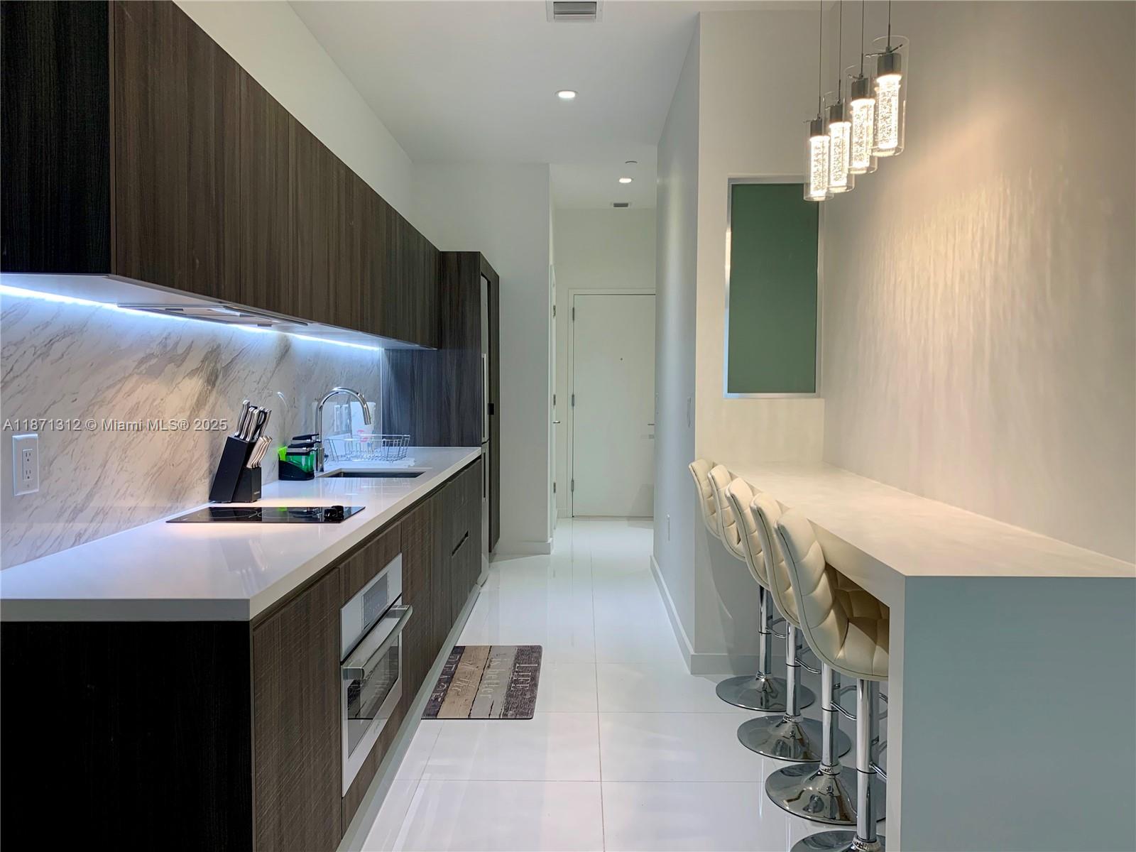 A modern kitchen features dark wood cabinetry, white countertops, and a breakfast bar with stools — 851 NE 1 Ave # 502, Miami FL 33132, MIAMI, FL