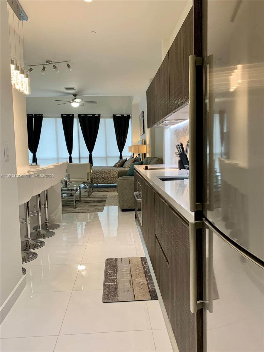 A modern kitchen with dark wood cabinets and white countertops overlooks a living area — 851 NE 1 Ave # 502, Miami FL 33132, MIAMI, FL