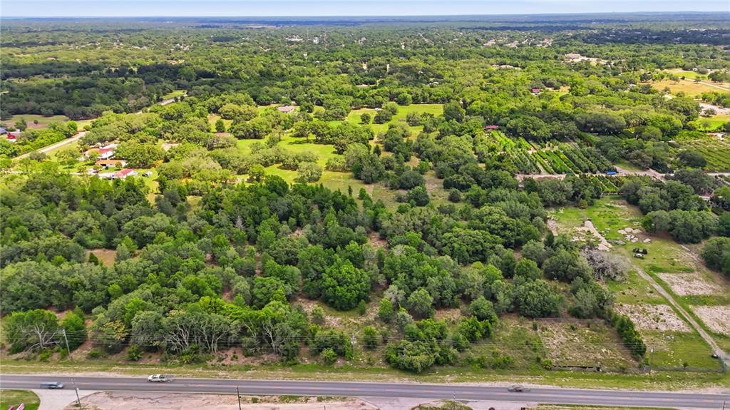 An aerial view shows a large, wooded plot of land bordering a paved road — 9433 COUNTY LINE ROAD, SPRING HILL, FL