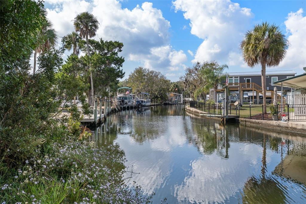 A canal view features docked boats, palm trees, and residential homes along the water — 10199 W BLUE SPRINGS COURT, HOMOSASSA, FL