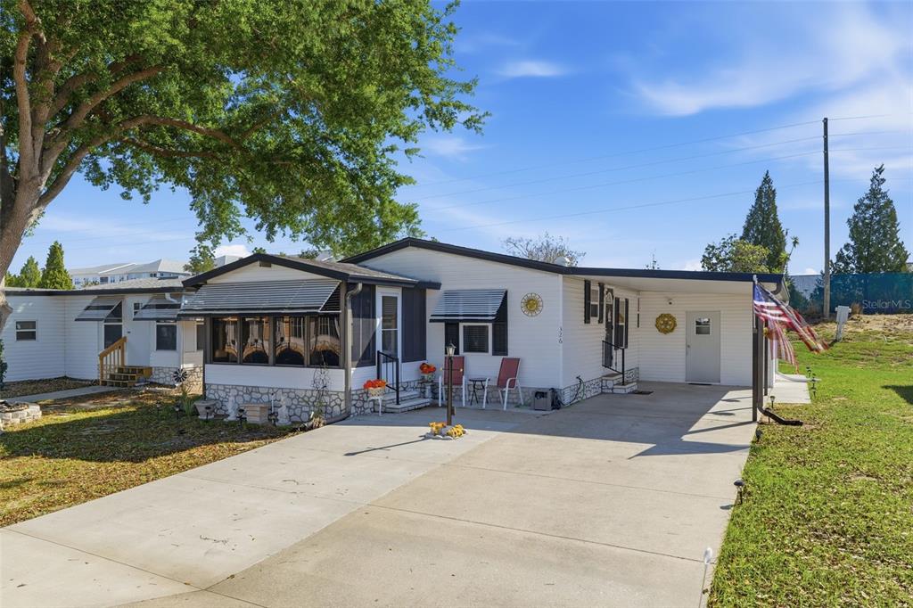 A white manufactured home features a concrete driveway, a carport, and a screened-in front porch — 326 NESBITT PARK AVENUE, DAVENPORT, FL