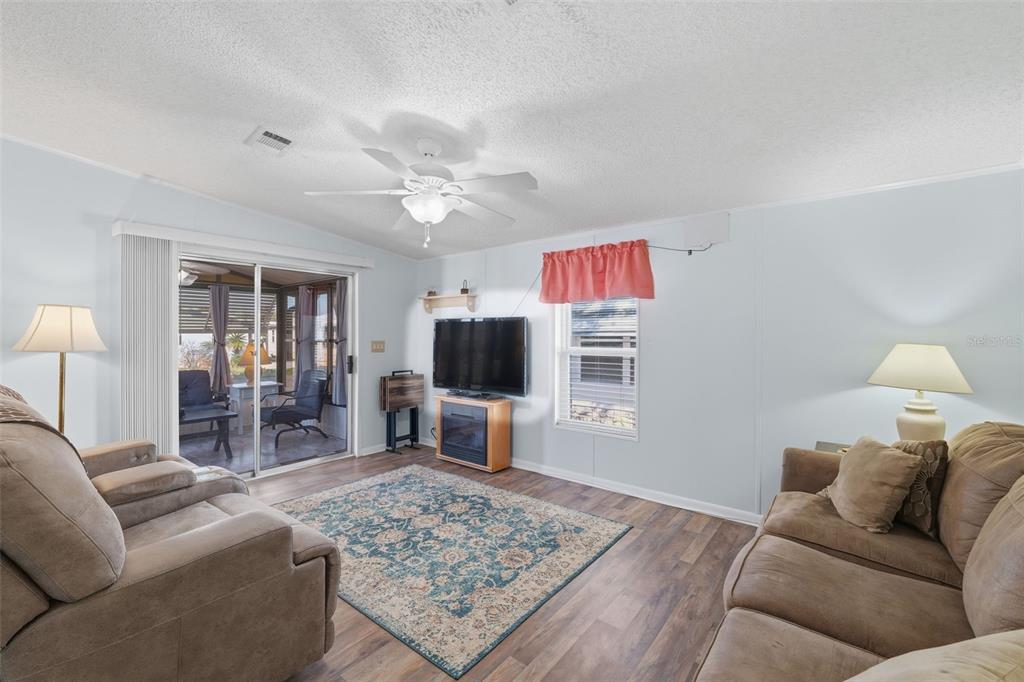 A living room features light blue walls, wood-look flooring, a ceiling fan, and sliding glass doors — 326 NESBITT PARK AVENUE, DAVENPORT, FL