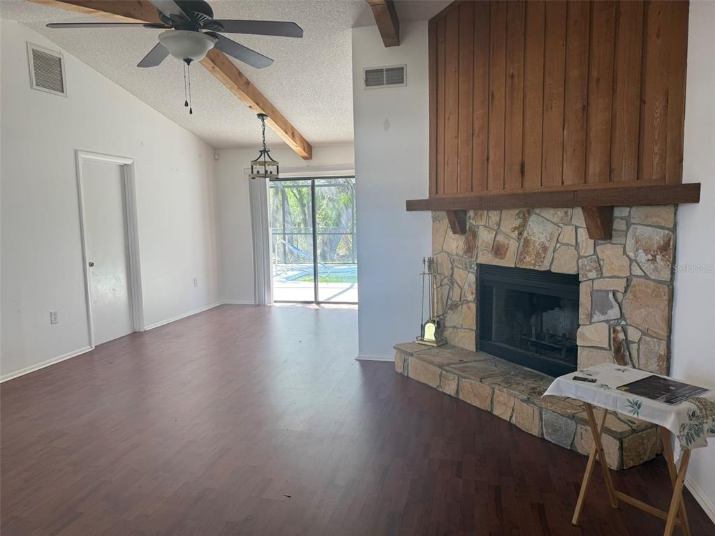 A living room features wood-look flooring, a stone fireplace, and a vaulted ceiling with beams — 2332 SEWARD DRIVE, SARASOTA, FL