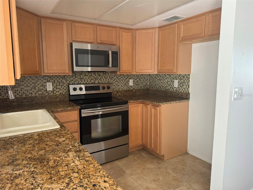 A kitchen features light wood cabinets, granite countertops, a mosaic backsplash, and stainless steel appliances — 2332 SEWARD DRIVE, SARASOTA, FL