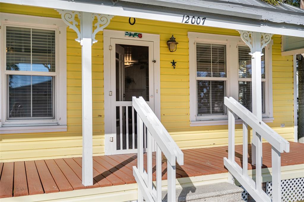 A yellow house exterior features a wooden porch, white railings, and a screen door — 12007 45TH AVENUE W, CORTEZ, FL