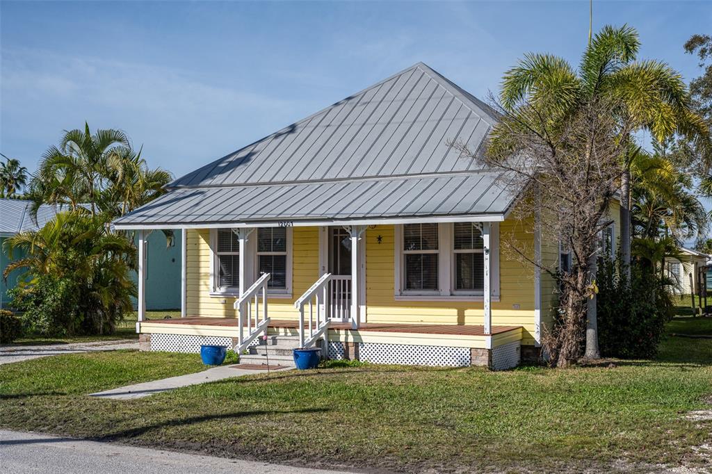 A yellow cottage with a metal roof and a front porch sits on a lawn — 12007 45TH AVENUE W, CORTEZ, FL