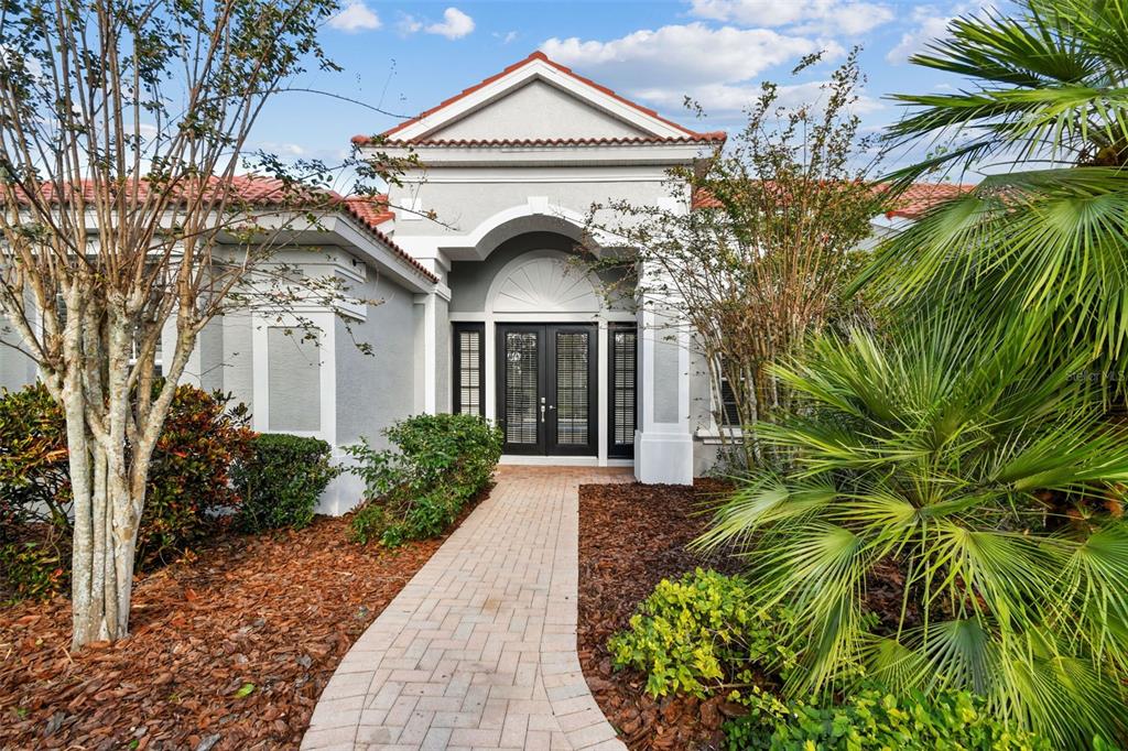The exterior of a house features a paved walkway leading to a double front door — 6815 HONEYSUCKLE TRAIL, LAKEWOOD RANCH, FL