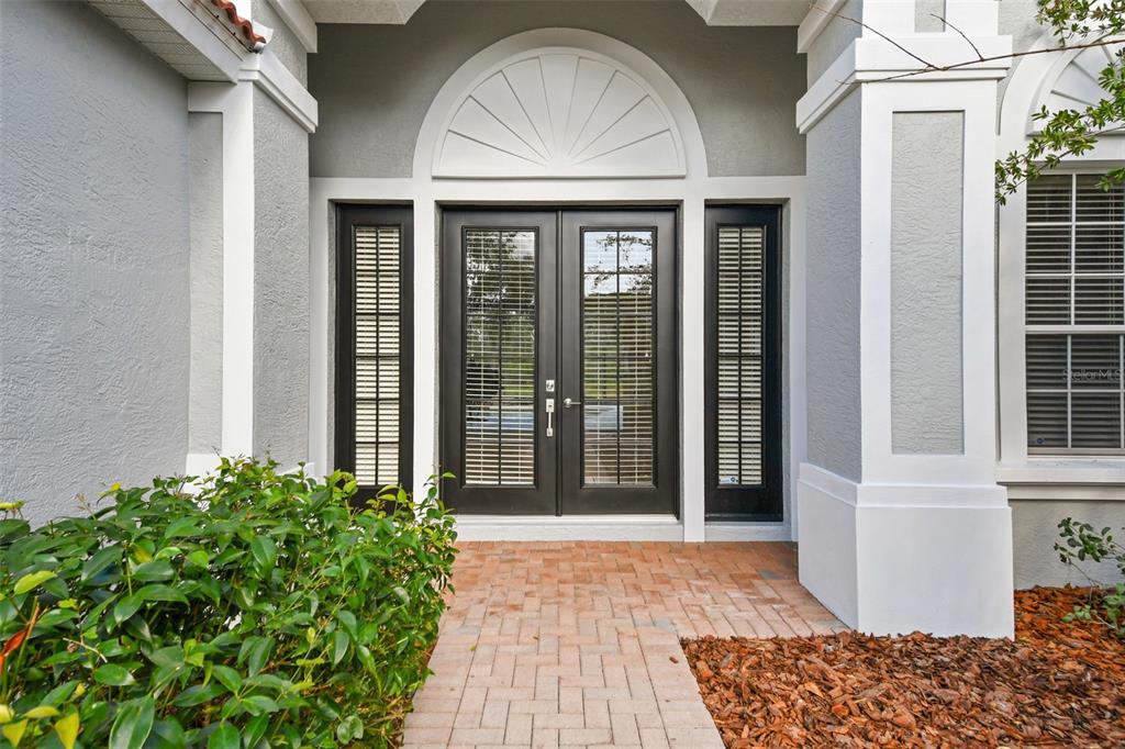 A front entryway features double glass doors with side panels and a semi-circular transom window — 6815 HONEYSUCKLE TRAIL, LAKEWOOD RANCH, FL