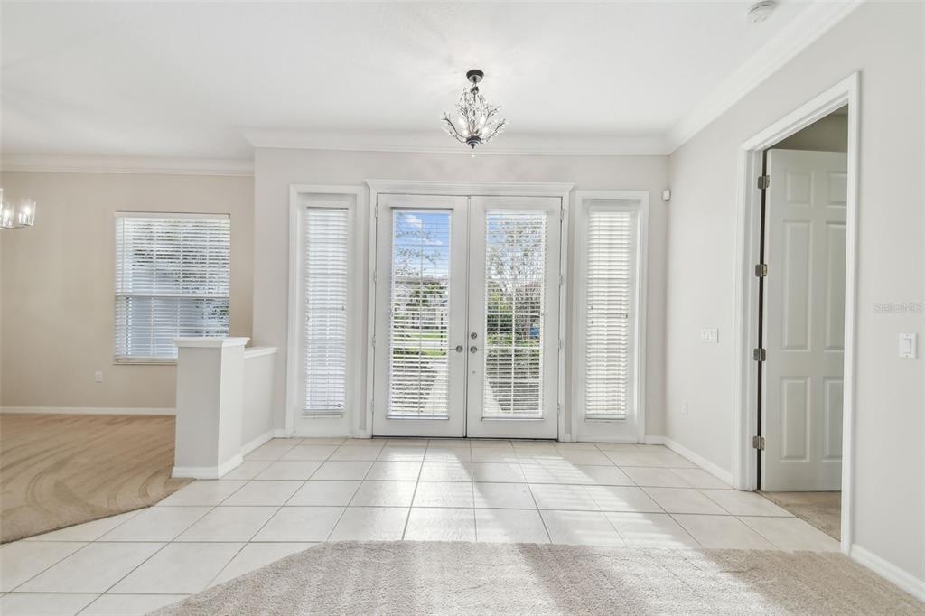 A bright room features white tile flooring, double glass doors, and a small crystal chandelier — 6815 HONEYSUCKLE TRAIL, LAKEWOOD RANCH, FL