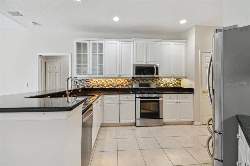 A kitchen with white cabinets, black countertops, stainless steel appliances, and a tiled floor — 6815 HONEYSUCKLE TRAIL, LAKEWOOD RANCH, FL