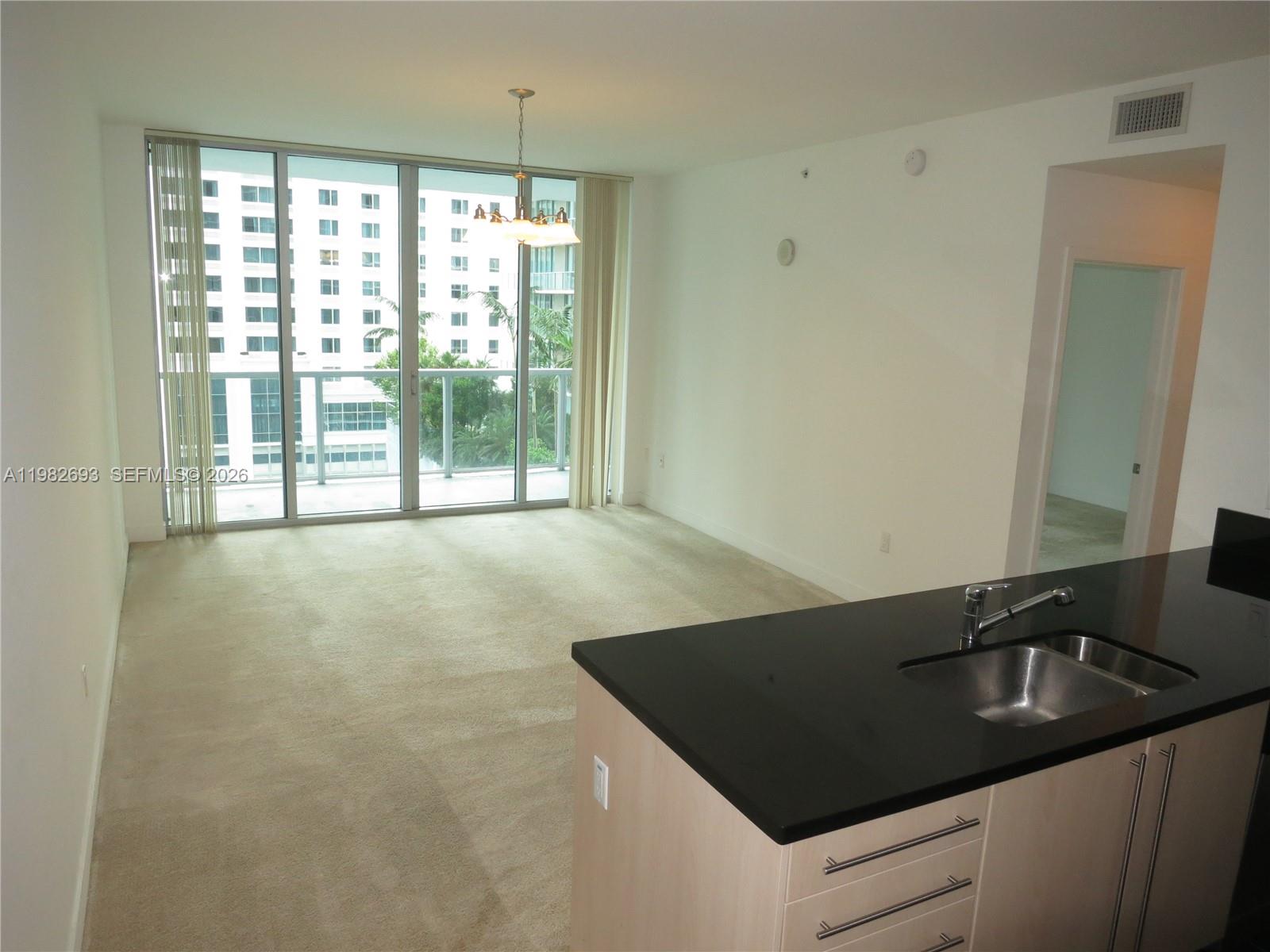 An open living area features beige carpeting, floor-to-ceiling windows, and a kitchen island with black countertops — 1111 SW 1 AV, Miami FL 33130, MIAMI, FL