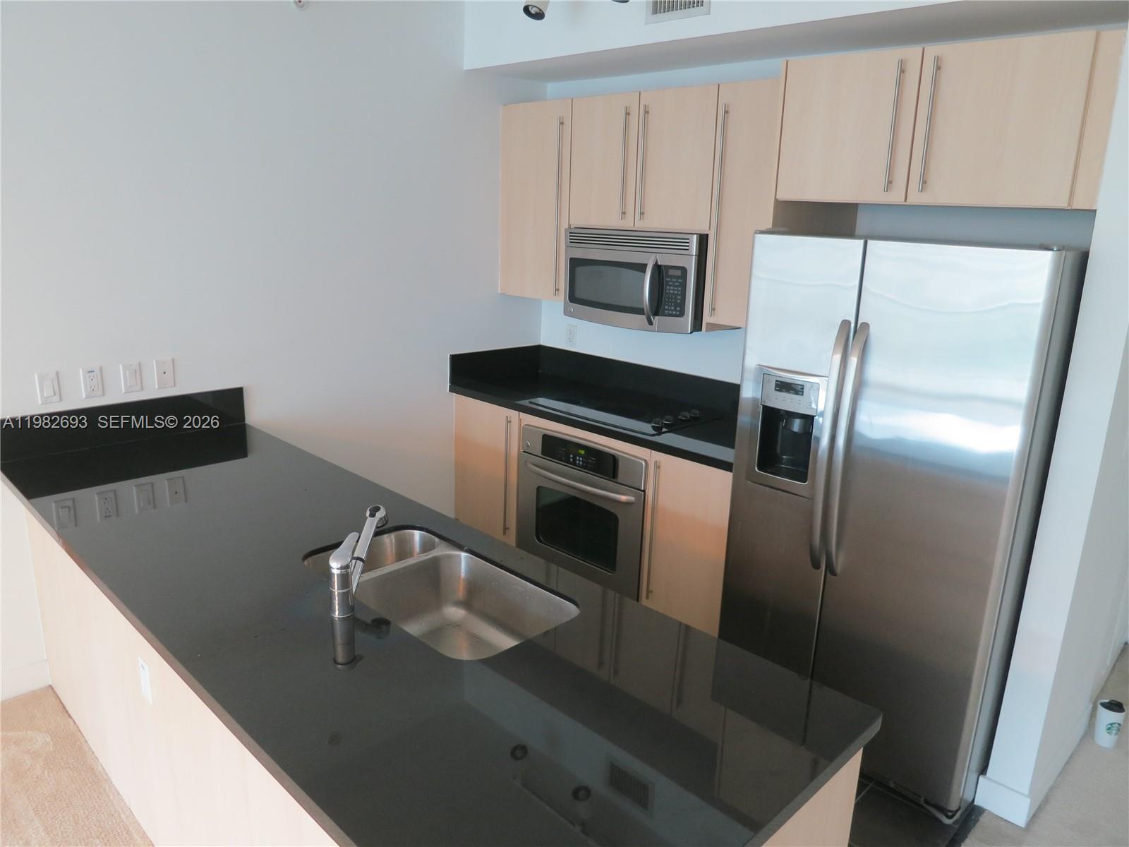 A kitchen features light wood cabinets, black countertops, stainless steel appliances, and a breakfast bar — 1111 SW 1 AV, Miami FL 33130, MIAMI, FL