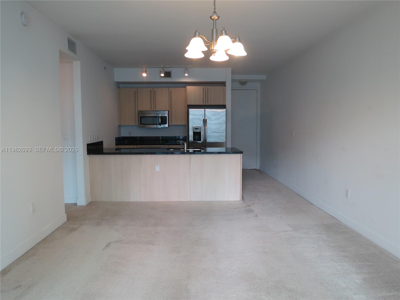 A kitchen with light wood cabinets and black countertops overlooks an open carpeted living area — 1111 SW 1 AV, Miami FL 33130, MIAMI, FL