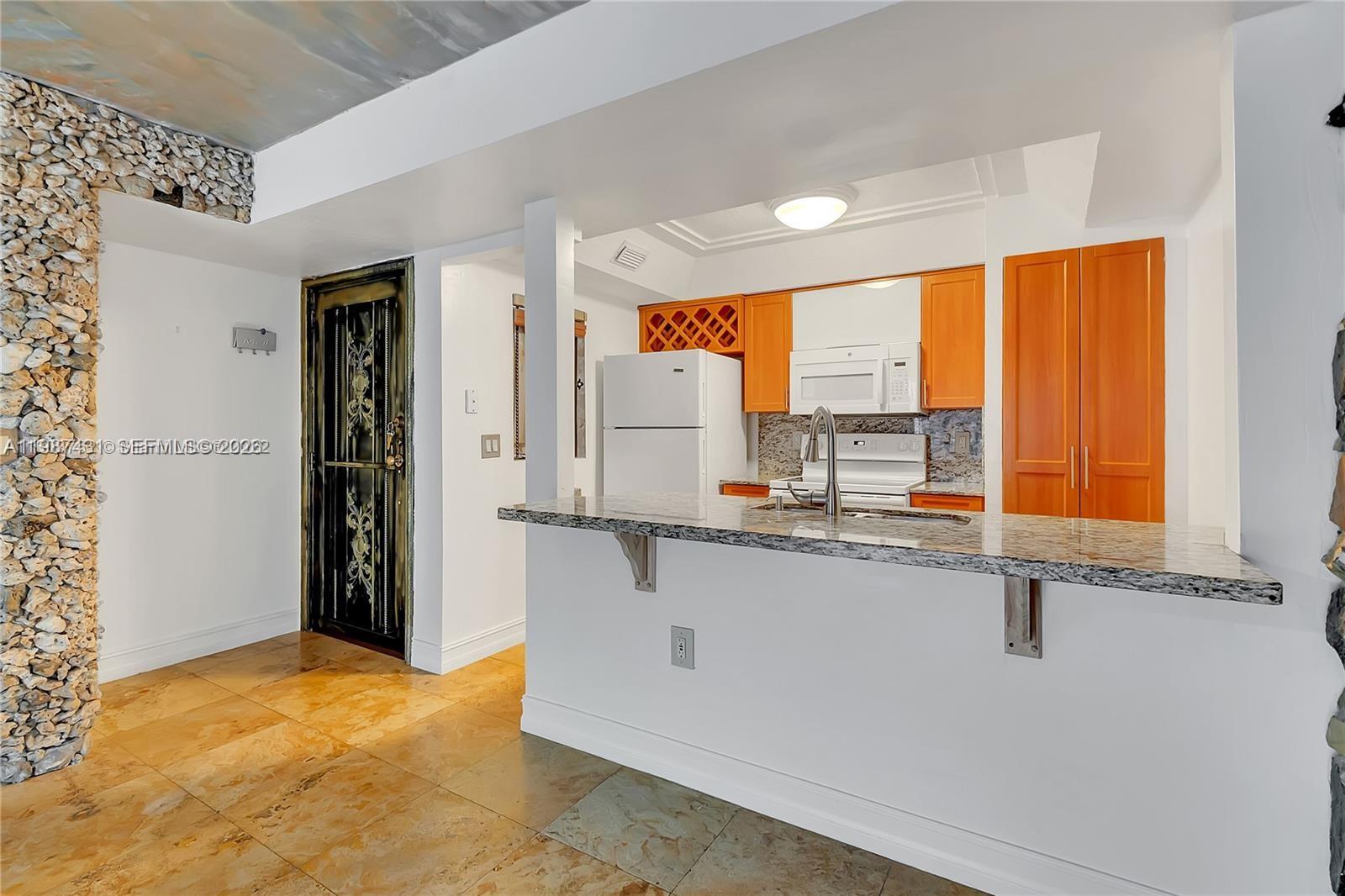 A kitchen features a granite breakfast bar, wooden cabinets, and a stone-textured accent wall — 6580 W 27th Ct # 12, Hialeah FL 33016, HIALEAH, FL