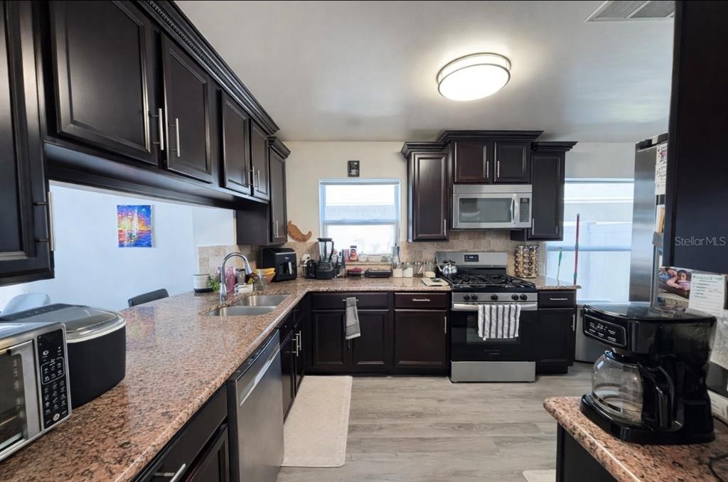 A kitchen features dark wood cabinets, granite countertops, stainless steel appliances, and light wood flooring — 2217 PAPRIKA DRIVE, ORLANDO, FL