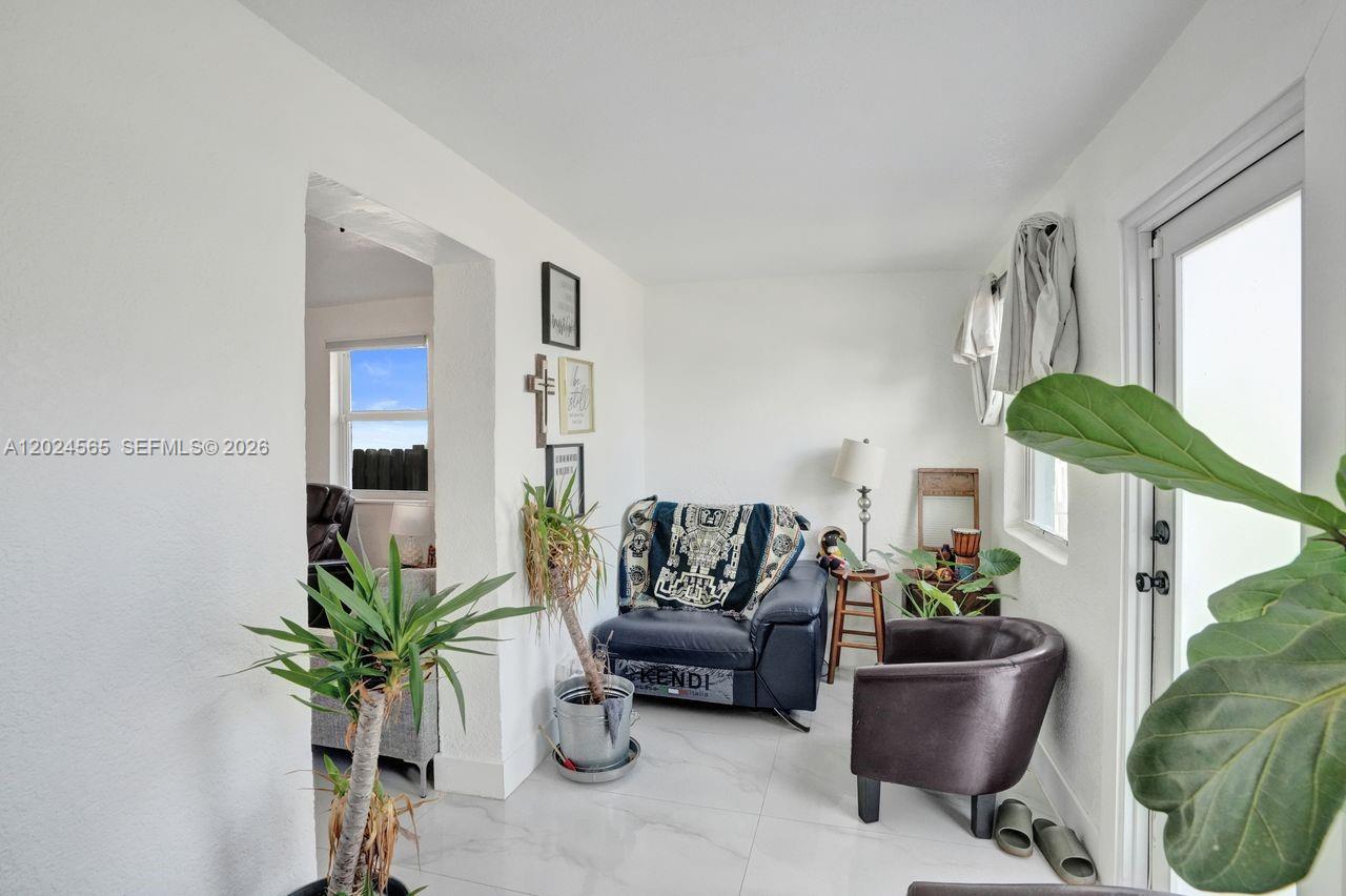 A sunroom features white walls, tile flooring, a blue armchair, and a dark accent chair — 2220 Hope St, Hollywood FL 33020, HOLLYWOOD, FL
