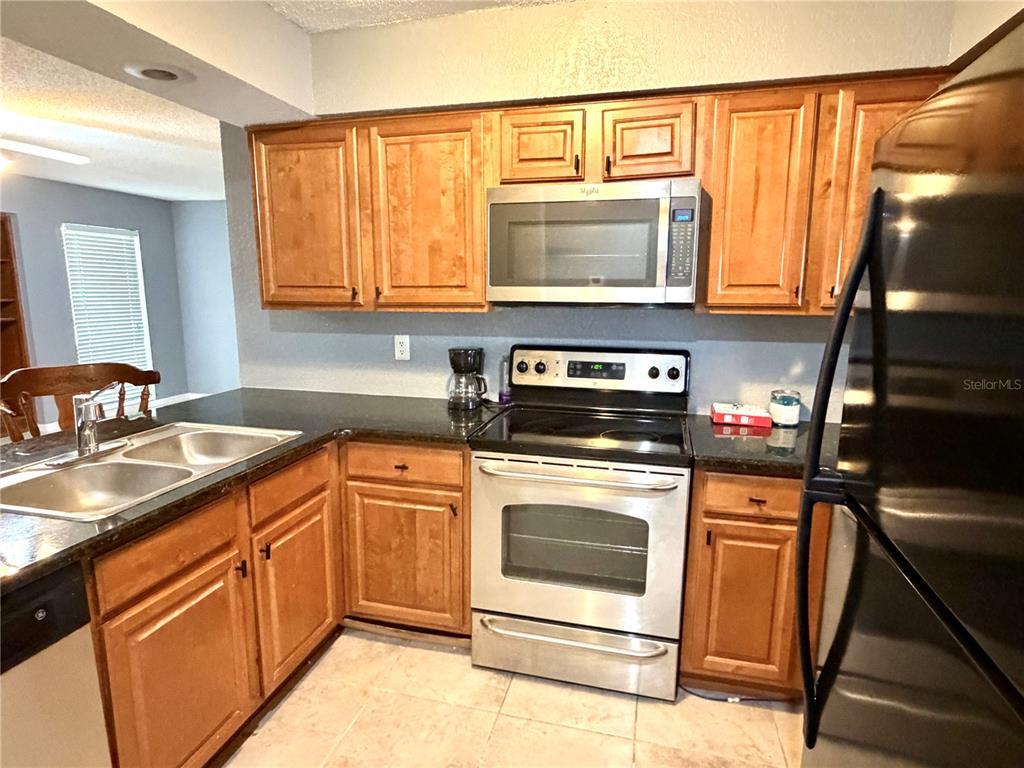 A kitchen features wood cabinets, stainless steel appliances, and dark countertops — 564 BRECKENRIDGE VILLAGE UNIT 106, ALTAMONTE SPRINGS, FL