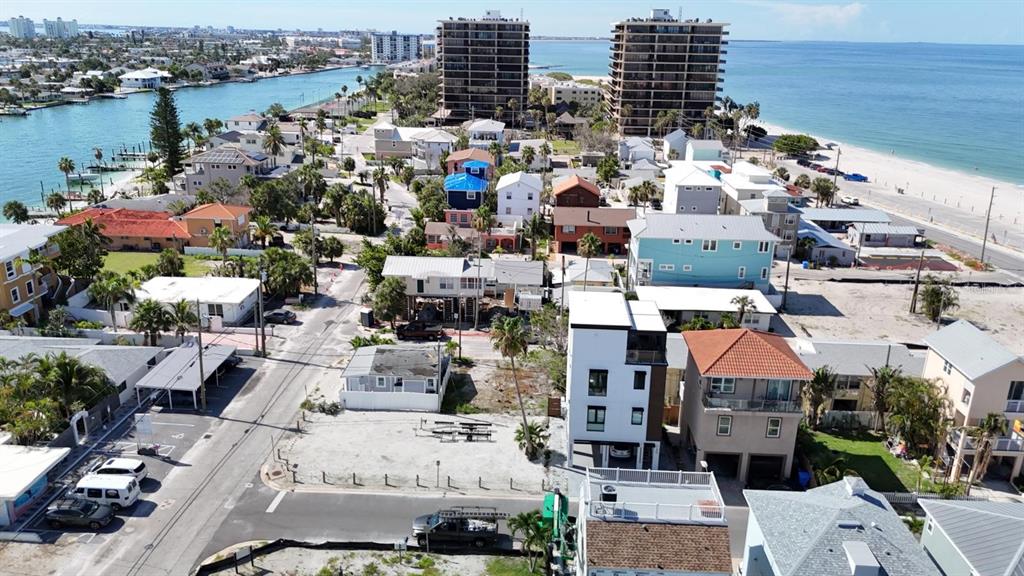 An aerial view shows a coastal neighborhood with houses, multi-story buildings, and a nearby beach — 37 80TH TERRACE, TREASURE ISLAND, FL