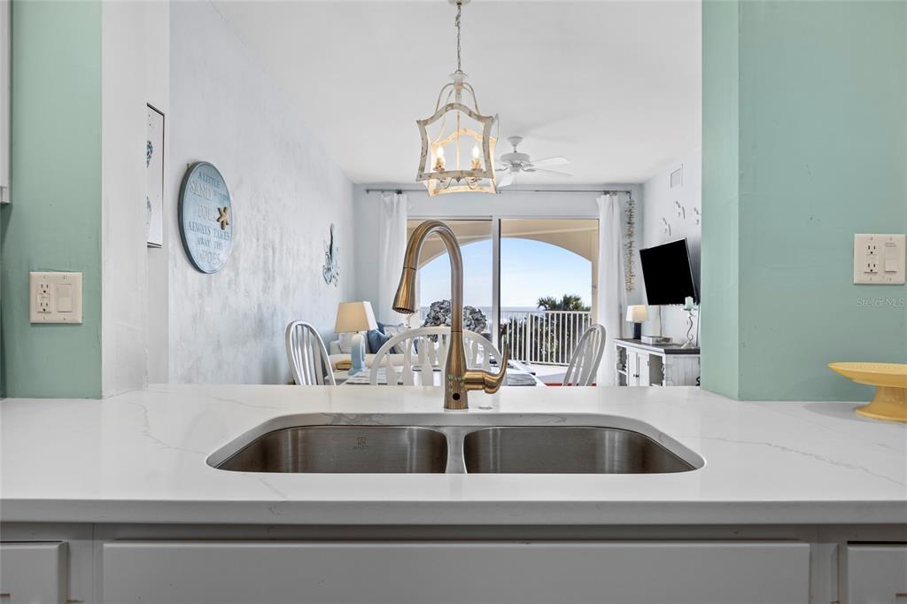 A kitchen sink with a gold faucet overlooks a dining area and a balcony view — 104 SURFVIEW DRIVE UNIT 2203, PALM COAST, FL