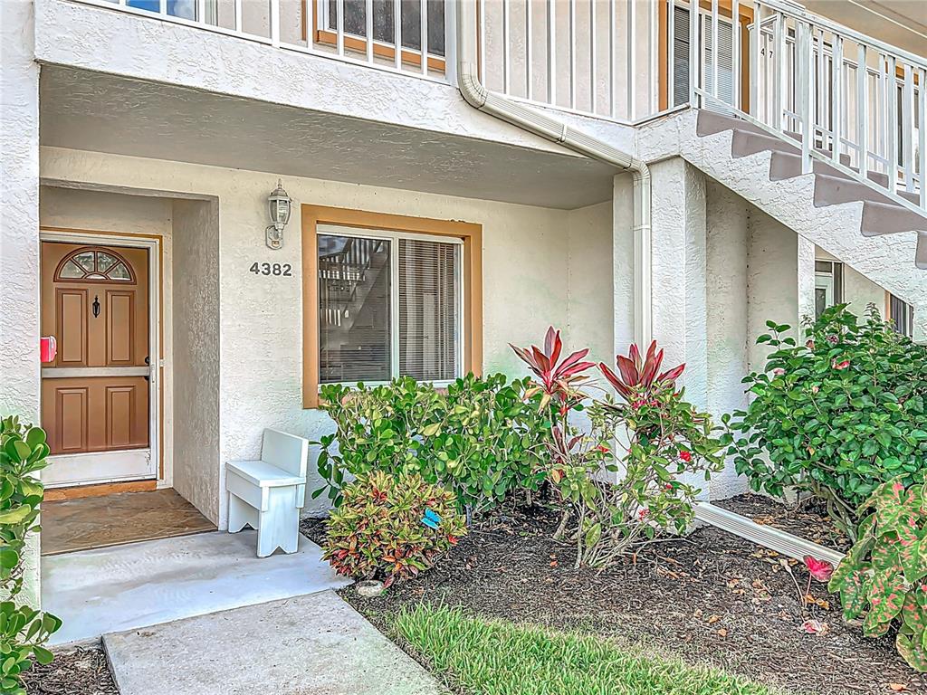 A ground-level apartment entrance features a brown door, a white bench, and landscaped garden beds — 4382 MADEIRA COURT UNIT 3361, SARASOTA, FL