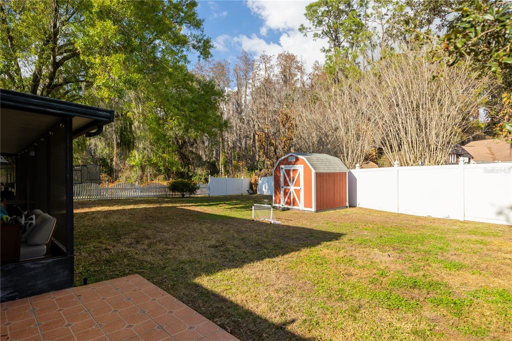 A backyard features a tiled patio, a grassy lawn, a storage shed, and white fencing — 3728 MURRAY DALE DRIVE, VALRICO, FL