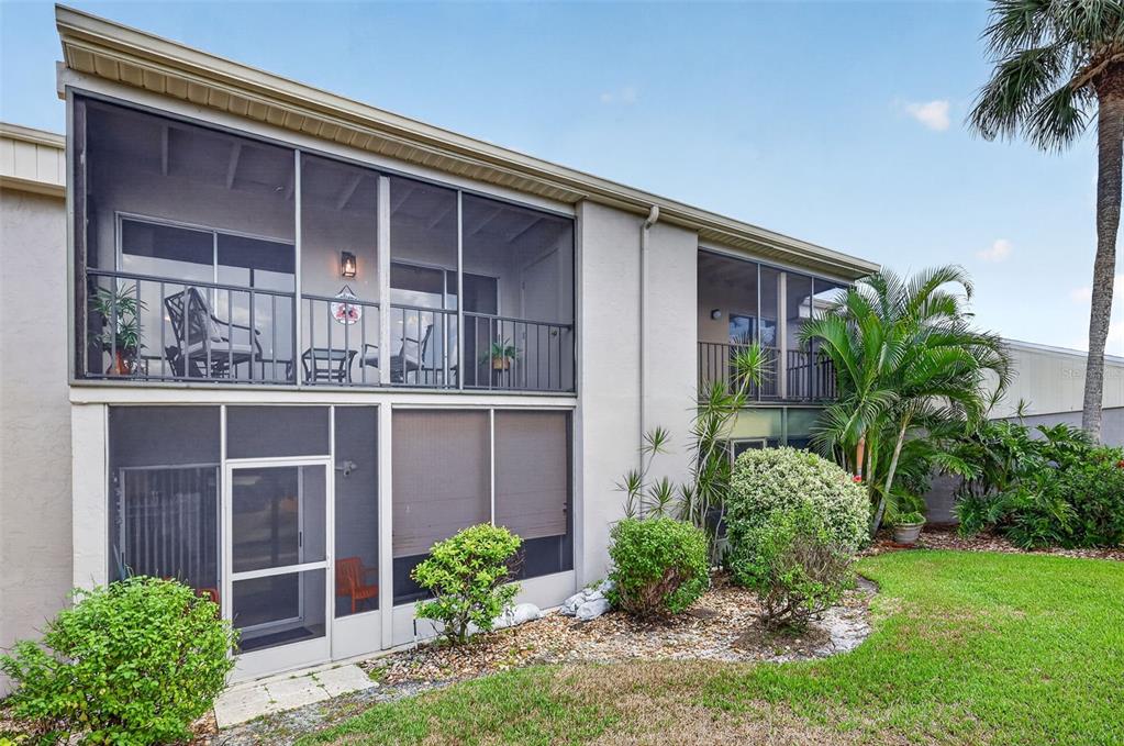 The exterior of a two-story building features screened-in balconies and patios overlooking a grassy yard — 6146 7TH AVENUE W UNIT 6146, BRADENTON, FL