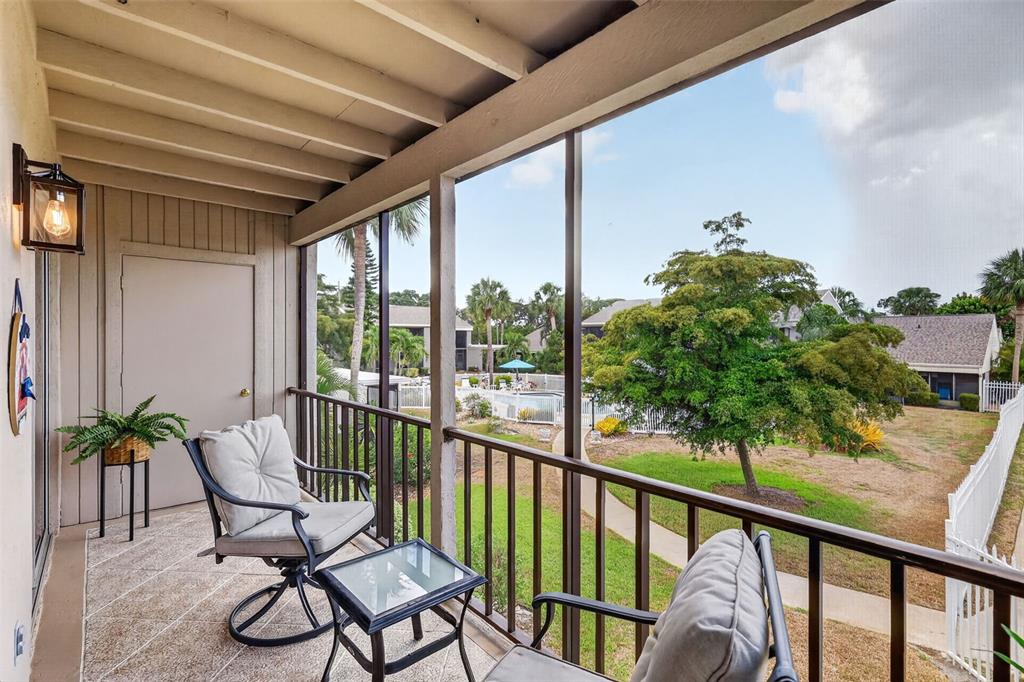 A screened-in balcony features a small table, two chairs, and a view of a pool — 6146 7TH AVENUE W UNIT 6146, BRADENTON, FL