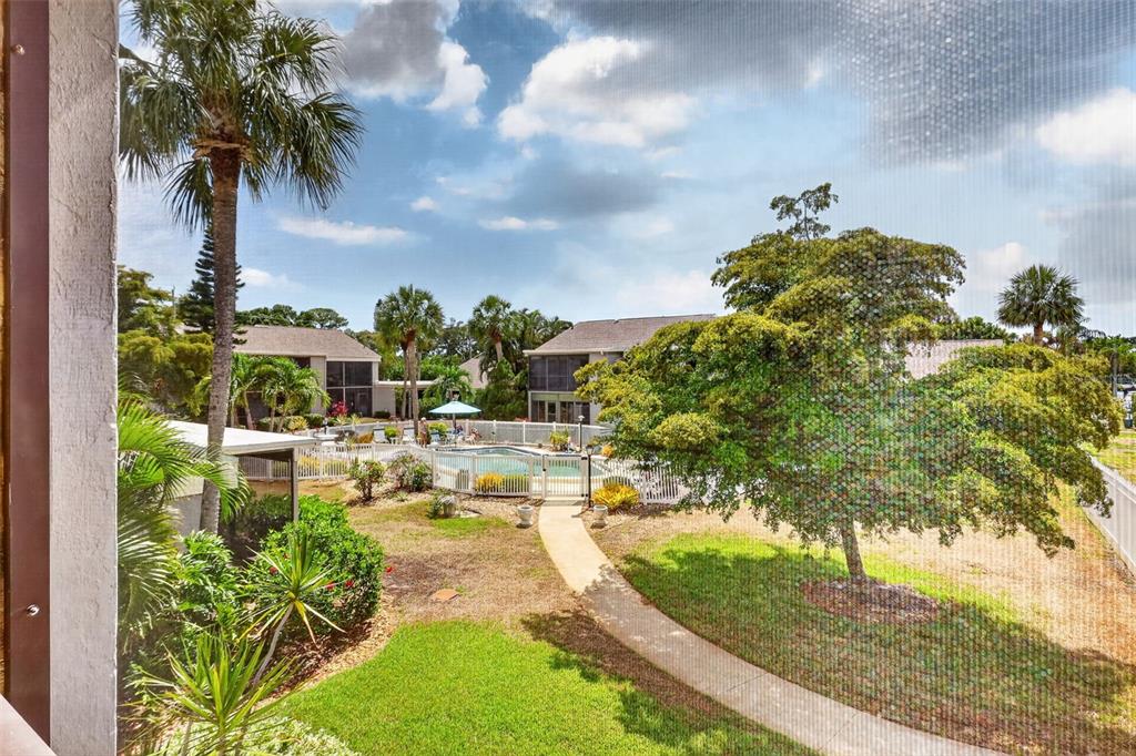 A view from a screened balcony overlooking a swimming pool, lawn, and palm trees — 6146 7TH AVENUE W UNIT 6146, BRADENTON, FL