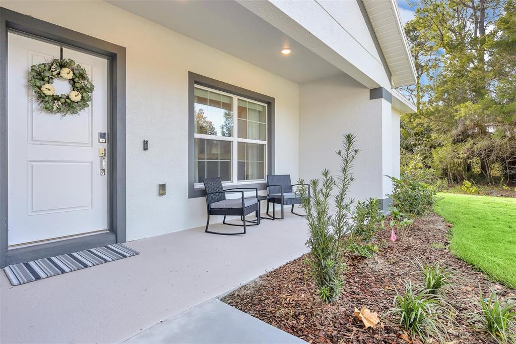 A covered front porch features a white door with a wreath, two chairs, and landscaping — 56 WHITE FEATHER LANE, PALM COAST, FL