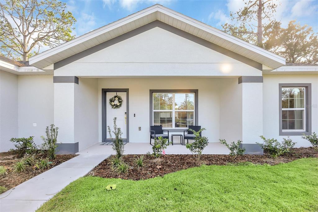 A front view of a white house with a covered porch, walkway, and landscaping — 56 WHITE FEATHER LANE, PALM COAST, FL