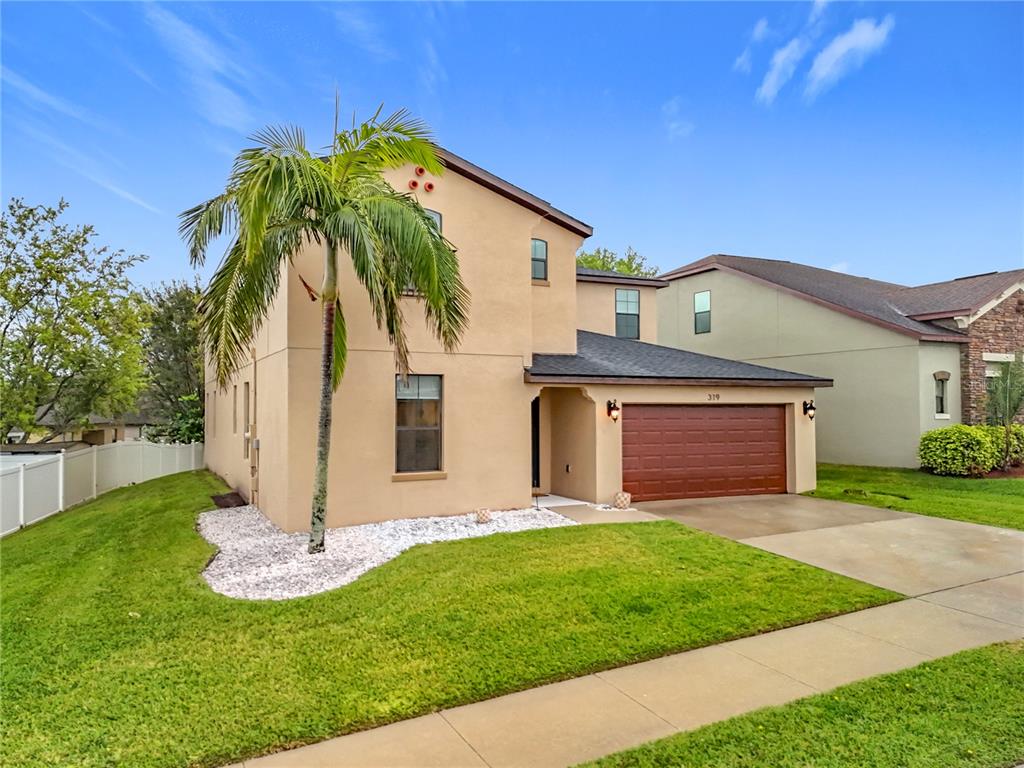 A two-story tan house with a palm tree, a brown garage door, and a grassy lawn — 319 ARBOR POINTE AVENUE, MINNEOLA, FL