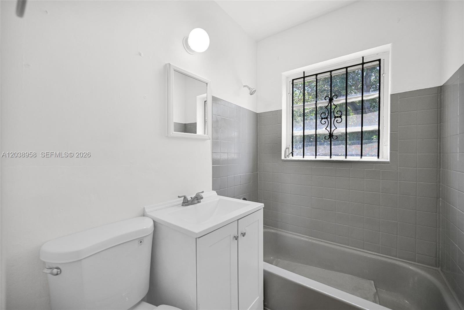 A bathroom features a white vanity, a toilet, and a bathtub with gray tiled walls — 5511 NW 12th Ave, Miami FL 33127, MIAMI, FL